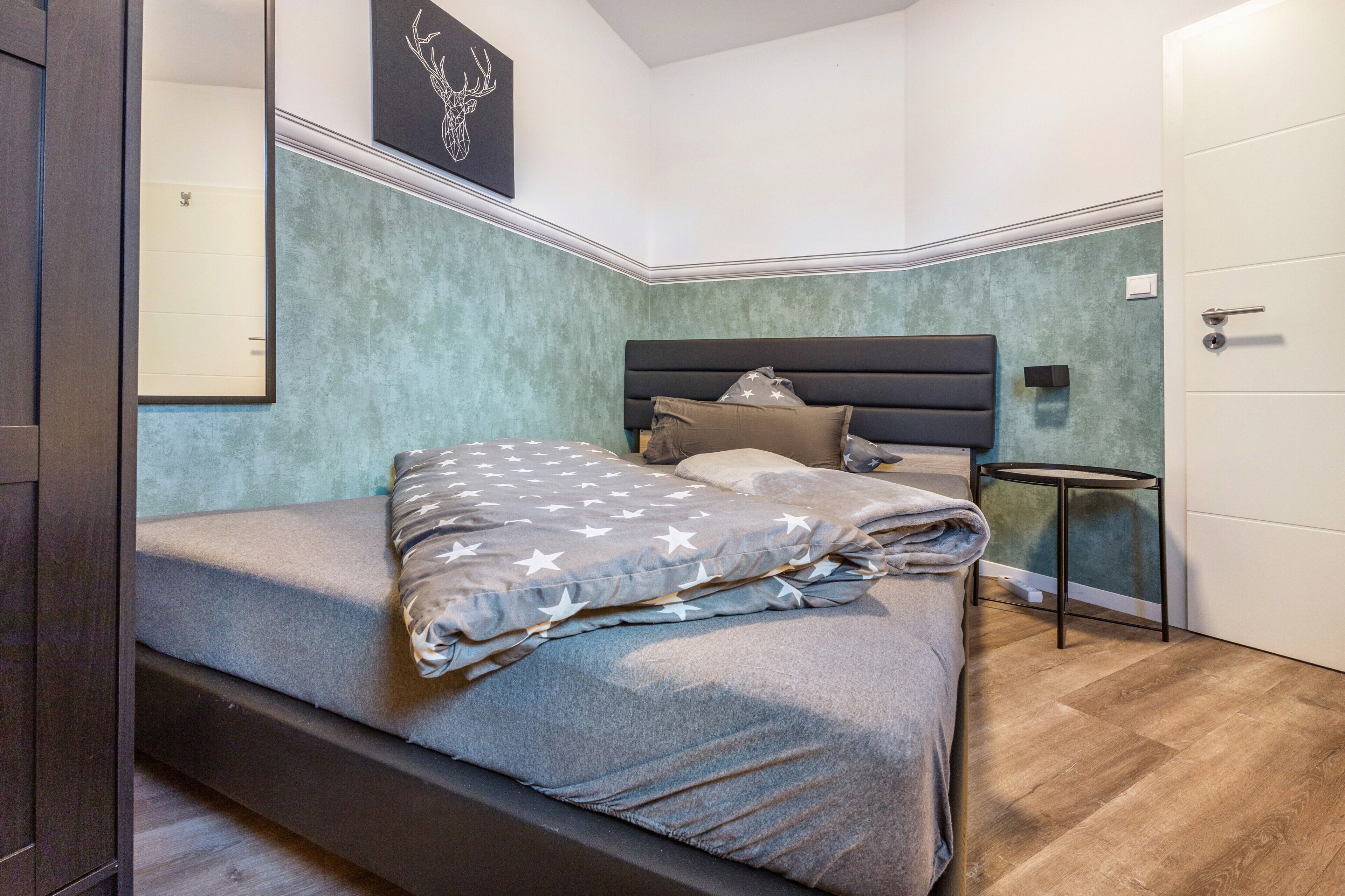 Een slaapkamer met een bed, nachtkastje, deur en een muur met een schilderij.