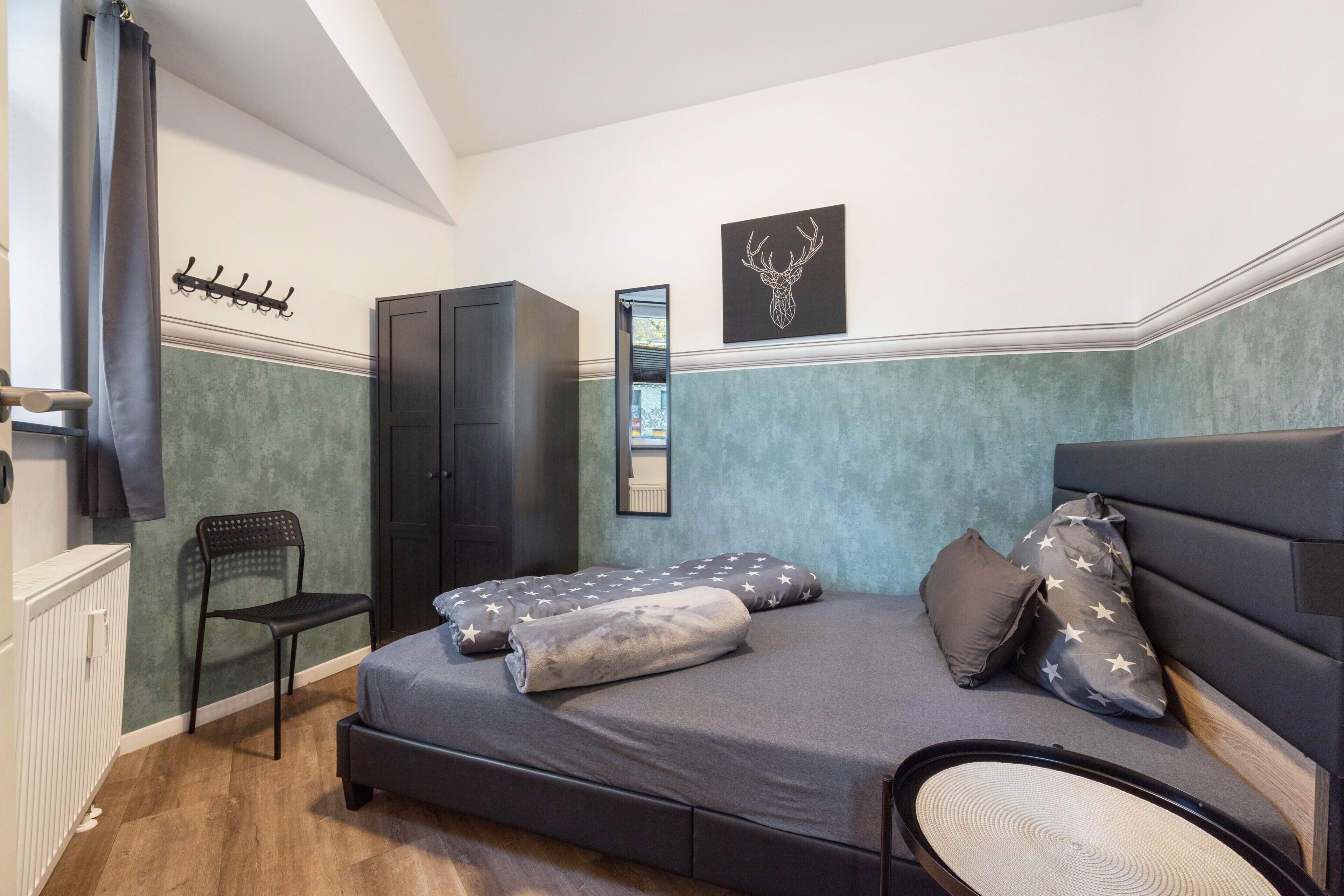A bedroom with a bed, a chair, a wardrobe, and a wall-mounted coat rack.