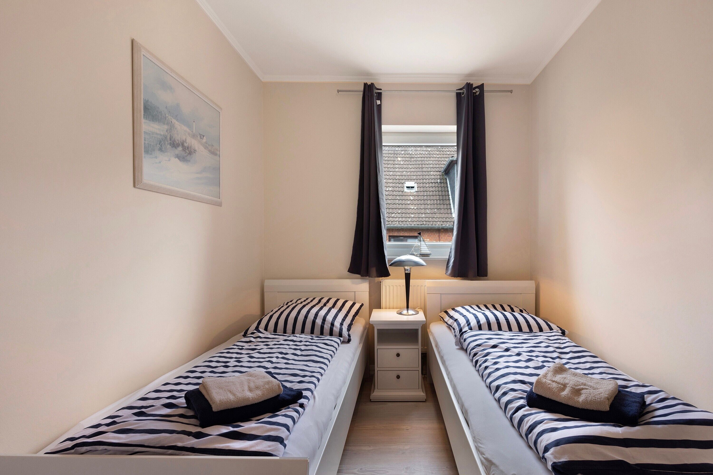 Un dormitorio con dos camas individuales, una mesita de noche, una lámpara y un ventanal con cortinas.