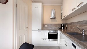 Eine kleine Küche mit weißen Schränken, einem Edelstahlbackofen, einem integrierten Geschirrspüler, einer Holz Arbeitsplatte und einem modernen Wasserhahn.