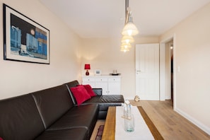 En stue med en sort lædersofa, et træsofabord, et indrammet maleri, et hvidt skab og en rød lampe.