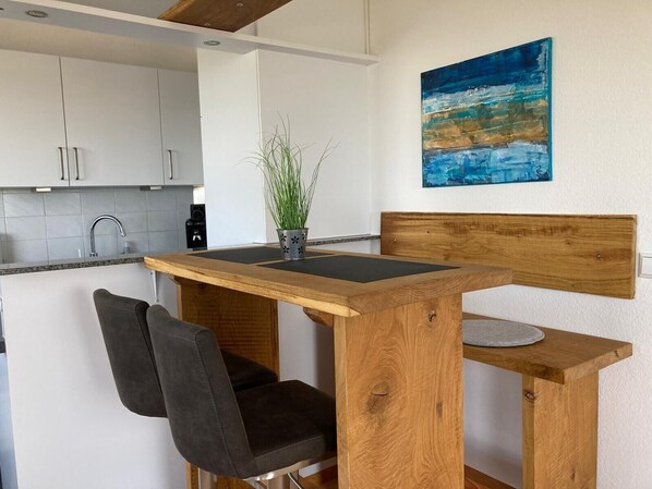 A modern kitchen with white cabinets, a wooden dining table, a black chair, and a potted plant.