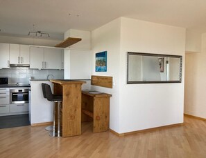 Une cuisine moderne avec des meubles blancs, une table à manger en bois et un grand miroir au mur.