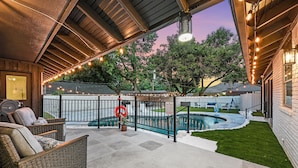 A covered patio area with outdoor seating, a swimming pool, and string lights.