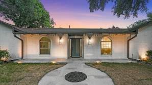 A two-story house with a front entrance, two large arched windows, and a circular driveway.