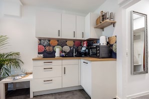 Une cuisine compacte avec des meubles blancs, un four à micro-ondes, une machine à café et un crédence décorative.