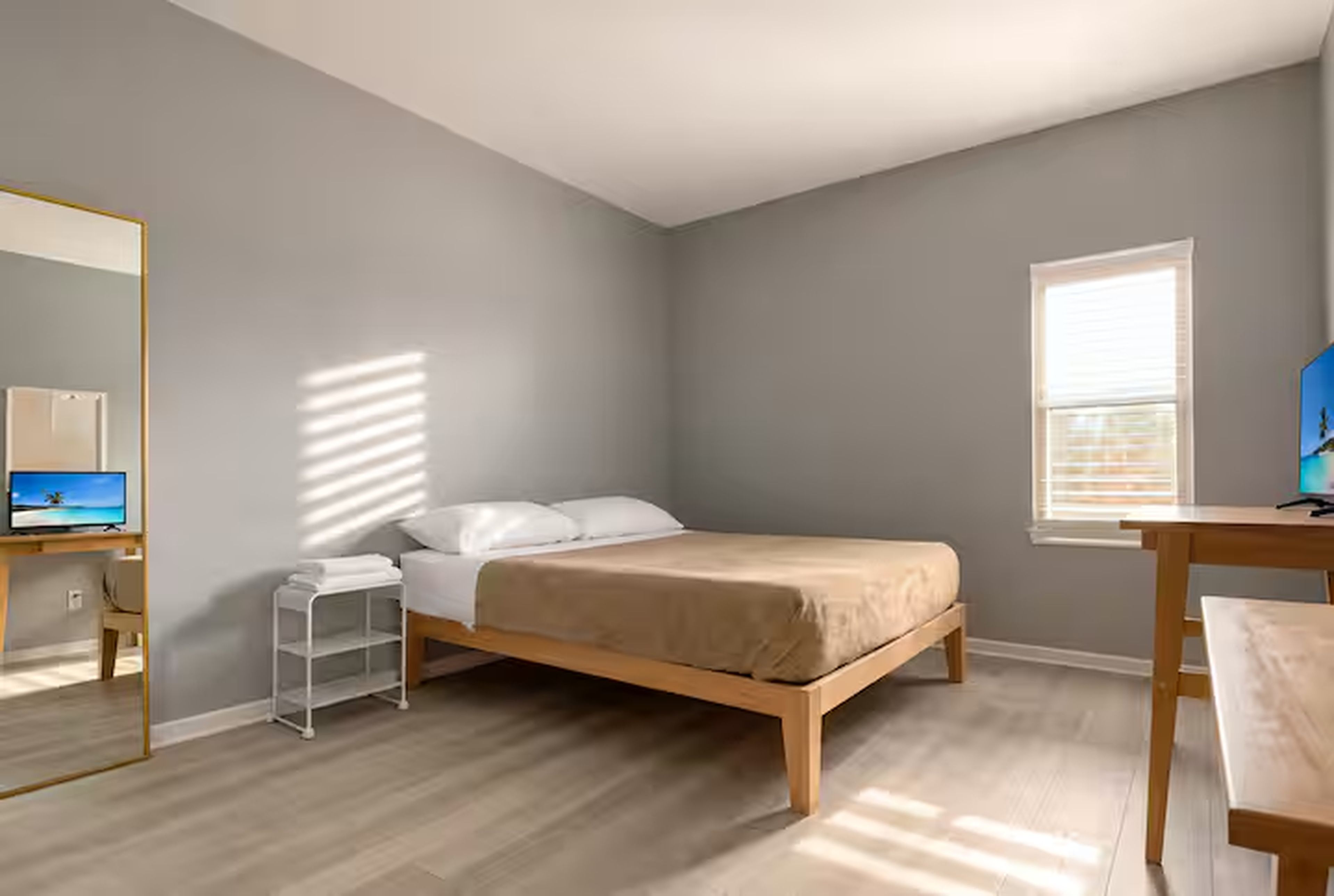 A bedroom with a bed, a desk, a chair, a mirror, and a window.