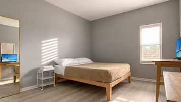 A bedroom with a bed, a desk, a chair, a mirror, and a window.