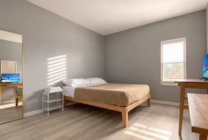 A bedroom with a bed, a desk, a chair, a mirror, and a window.