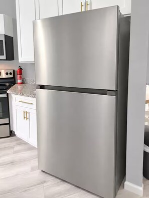 Ein Edelstahl-Kühlschrank in einer Küche mit weißen Schränken und einer Arbeitsplatte aus Granit.