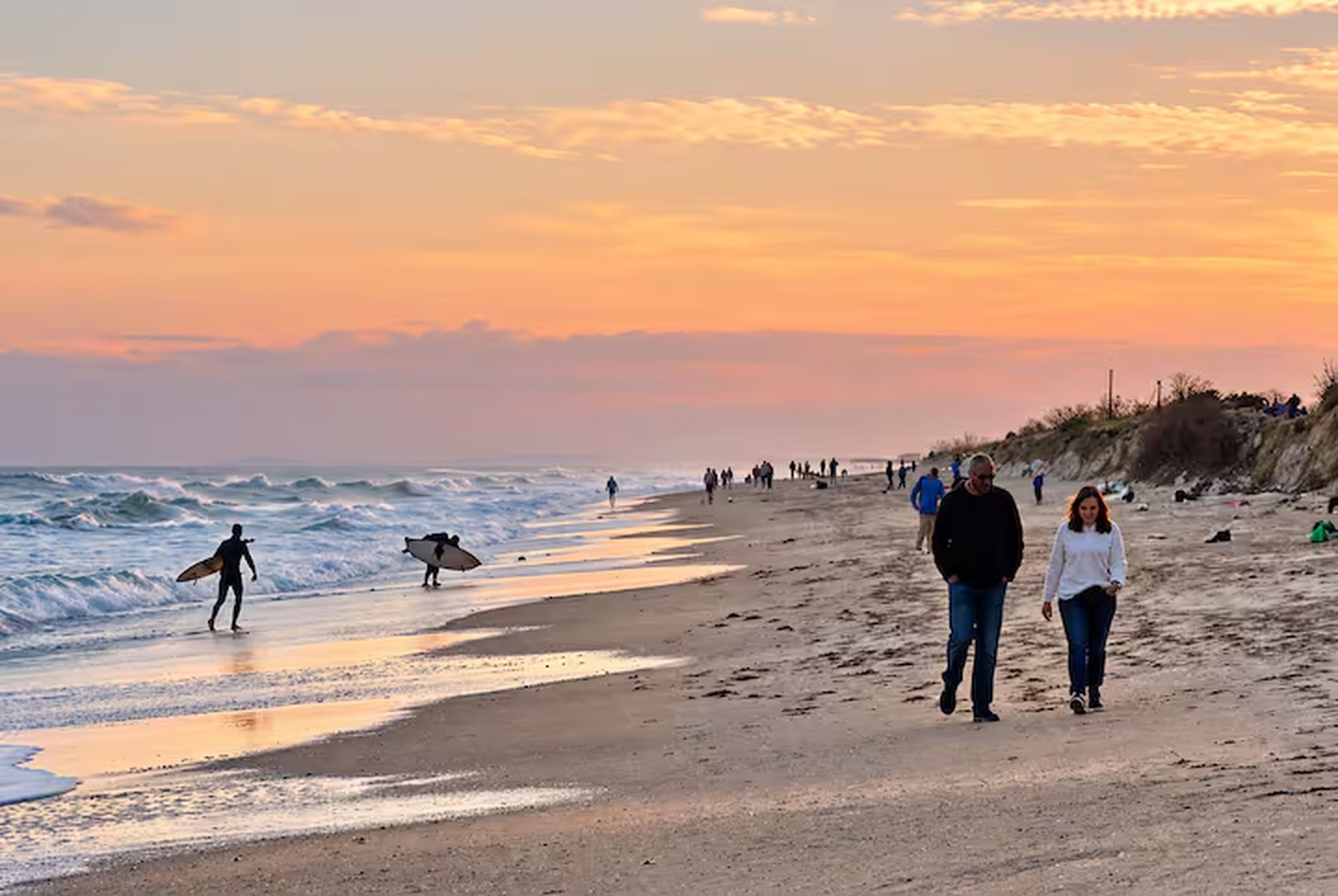 A beach with people walking and surfing, and the ocean in the background.