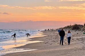 Ein Strand mit Menschen, die spazieren gehen und surfen, und der Ozean im Hintergrund.