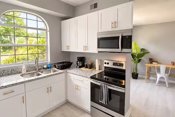 A modern kitchen with white cabinets, a stainless steel oven, a microwave, and a large window with a view of greenery.