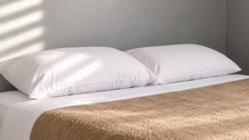 A bed with white bedding and a brown blanket.