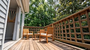 A wooden deck with a wooden fence, two wooden chairs, and a small table.