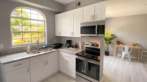 A kitchen with white cabinets, a large window, a microwave, an oven, and a small table with chairs.