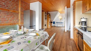 A dining area with a table set for four, a kitchen with wooden cabinets, and a brick wall. - Apartment 'Wohnung Auf Dem Dorf' with Wi-Fi (Zarpen)