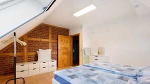A bedroom with a sloped ceiling, a brick wall, a wooden door, a bed with a blue and white striped bedspread, and a white dresser. - Apartment 'Wohnung Auf Dem Dorf' with Wi-Fi (Zarpen)