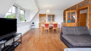A living room with a TV, sofa, dining table, chairs, and a chandelier. - Apartment 'Wohnung Auf Dem Dorf' with Wi-Fi (Zarpen)