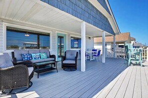 Relax on the covered deck with a sofa set and wicker chairs, surrounded by a white fence.
