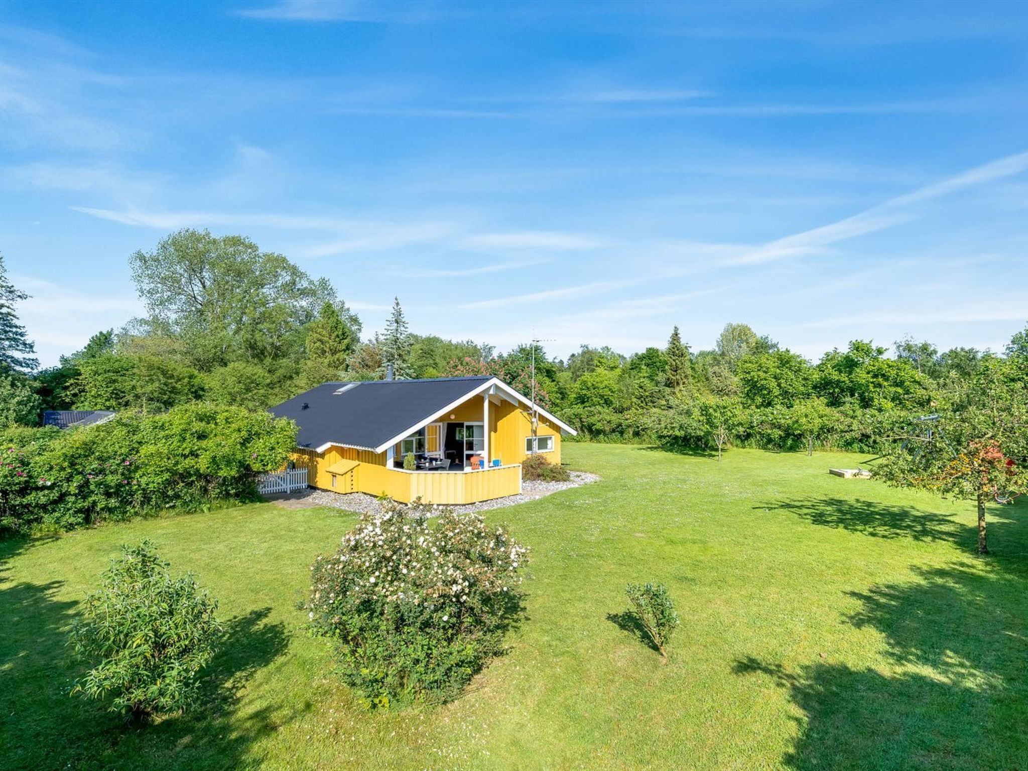 A yellow house with a black roof surrounded by a well-maintained lawn and various trees.