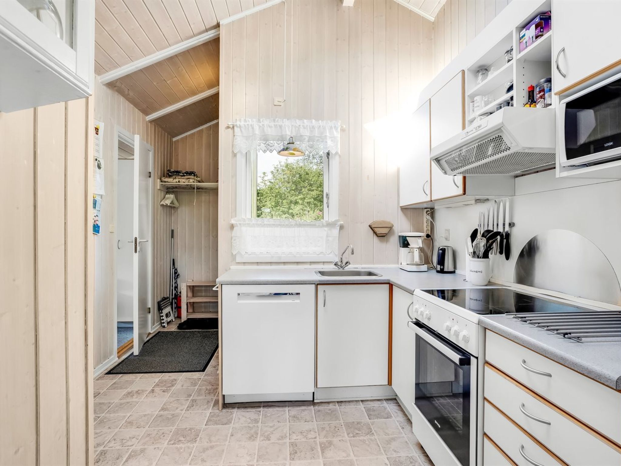 A compact kitchen with a window, white cabinets, a microwave, and a stove.