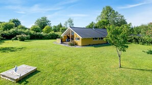 A small wooden house with a sloped roof, surrounded by a well-maintained lawn and trees. - "Guja" - 250m from the sea by Interhome (Faxe Ladeplads)