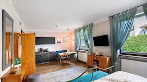 Une chambre à coucher comprenant un lit, un bureau, une chaise, un téléviseur et donnant sur un espace verdoyant.