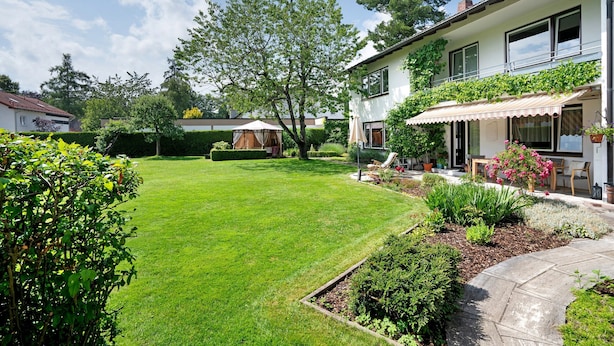 Un jardin bien entretenu, avec une pelouse, un chemin de pierres et une maison dotée d’un balcon.