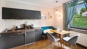 Une cuisine compacte dotée d’appareils électroménagers modernes, un coin repas avec une chaise bleue et une fenêtre donnant sur un paysage verdoyant.