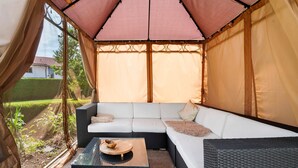 Un espace extérieur aménagé, abrité et doté d’un canapé et d’une table, entouré d’une pergola couverte.