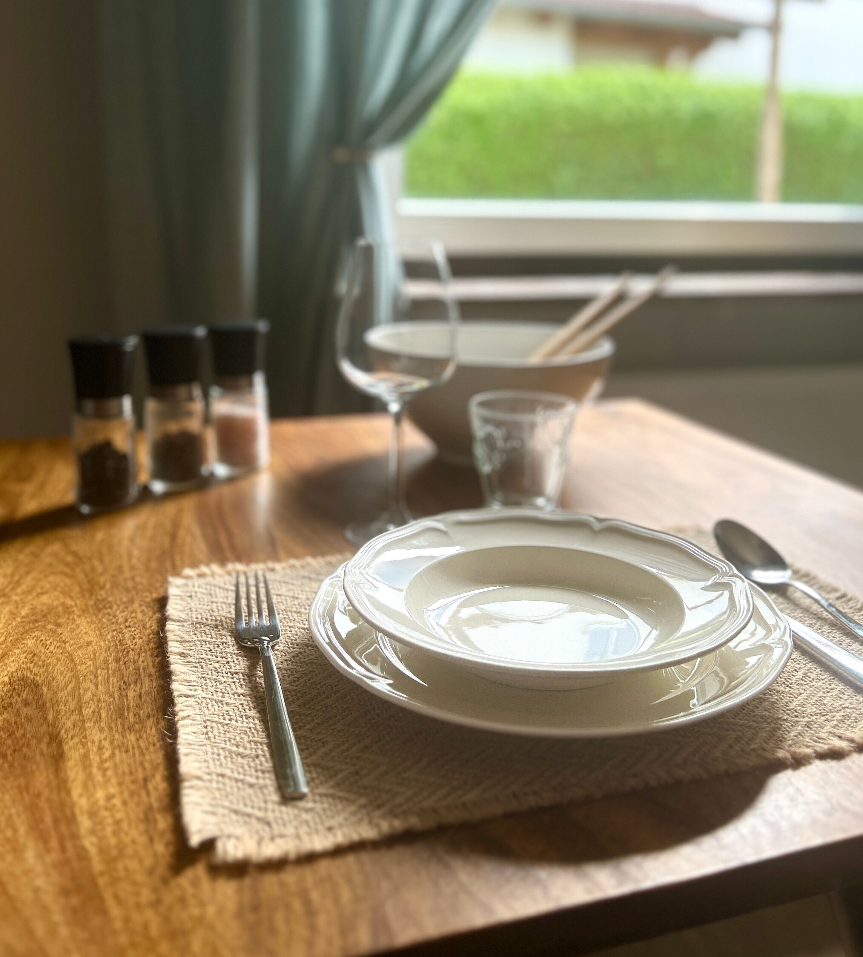 A dining table with a plate, fork, knife, and glass, set on a wooden table with a burlap placemat.