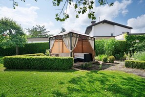 A well-maintained garden with a gazebo, neatly trimmed hedges, and a white building in the background.