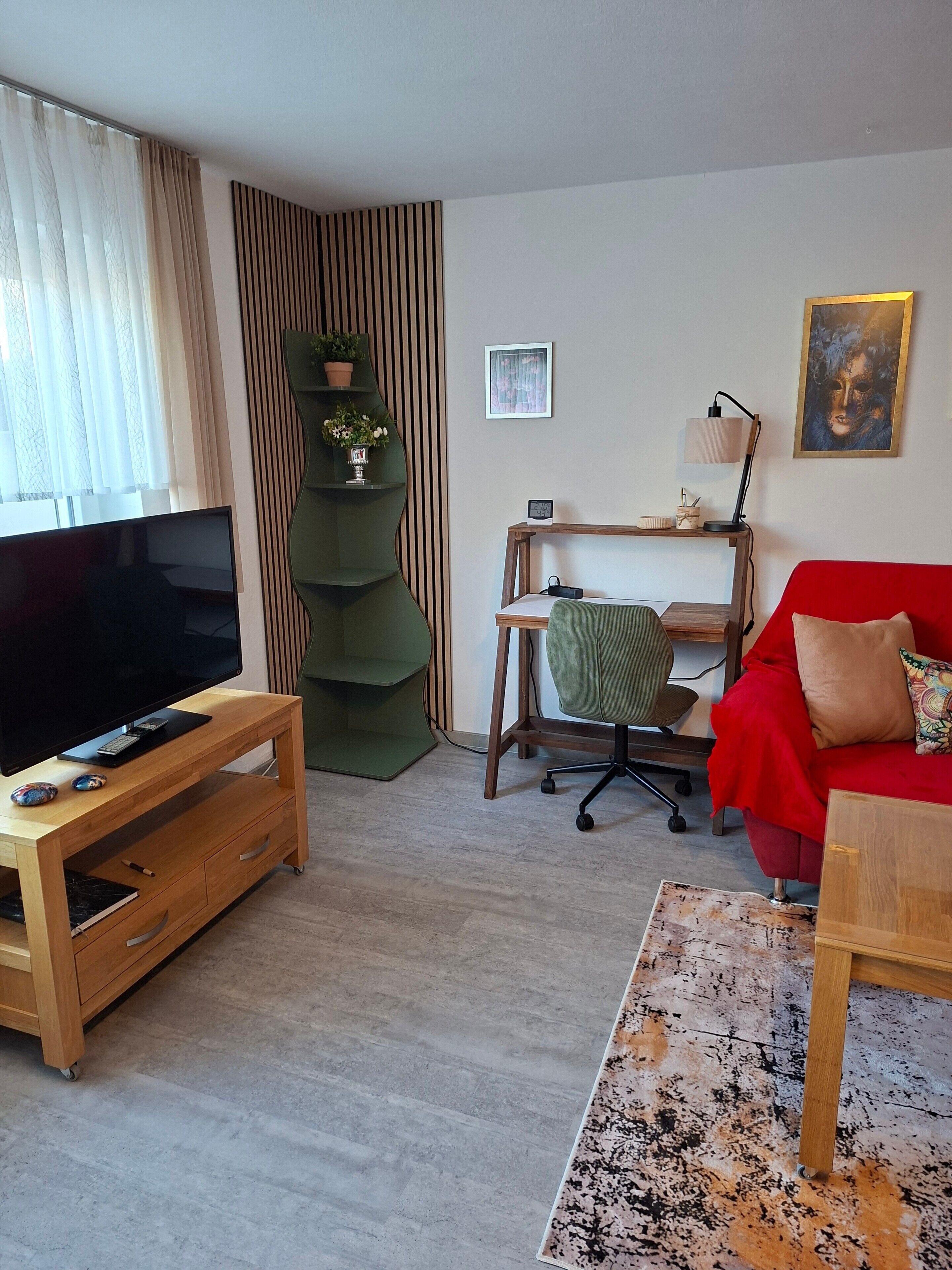 A living room with a TV, a red sofa, a wooden desk, and a green chair.
