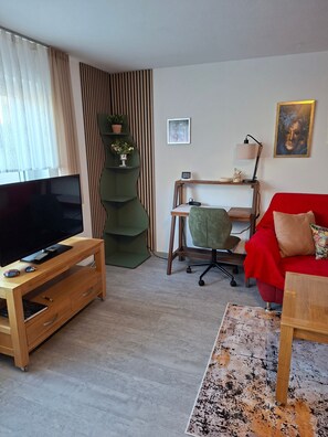 Ein Wohnzimmer mit Fernseher, einem roten Sofa, einem Holztisch und einem grünen Sessel.