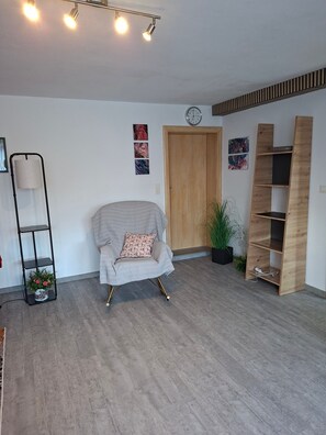A room with a wooden door, a chair with a cushion, a floor lamp, a shelf with plants, and a wall clock. - Apartment 'Collenberger Ferienwohnung Schäfer' with Private Terrace, Garden & Wi-Fi (Collenberg)