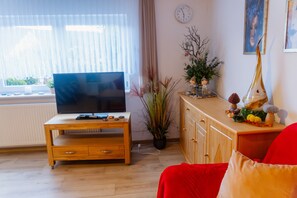 Un salon avec un meuble TV en bois, un canapé rouge, une plante en pot et un buffet orné d’objets décoratifs.