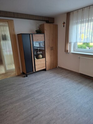 Una habitación con un armario de madera, un radiador y una ventana con cortinas traslúcidas.