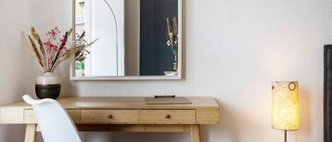 A wooden desk with a mirror, a vase with dried flowers, and a table lamp.