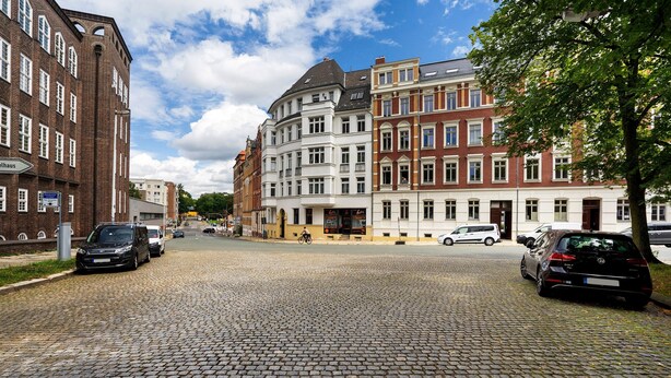 Eine Kopfsteinpflasterstraße gesäumt von historischen Gebäuden, einem Café und parkenden Autos.