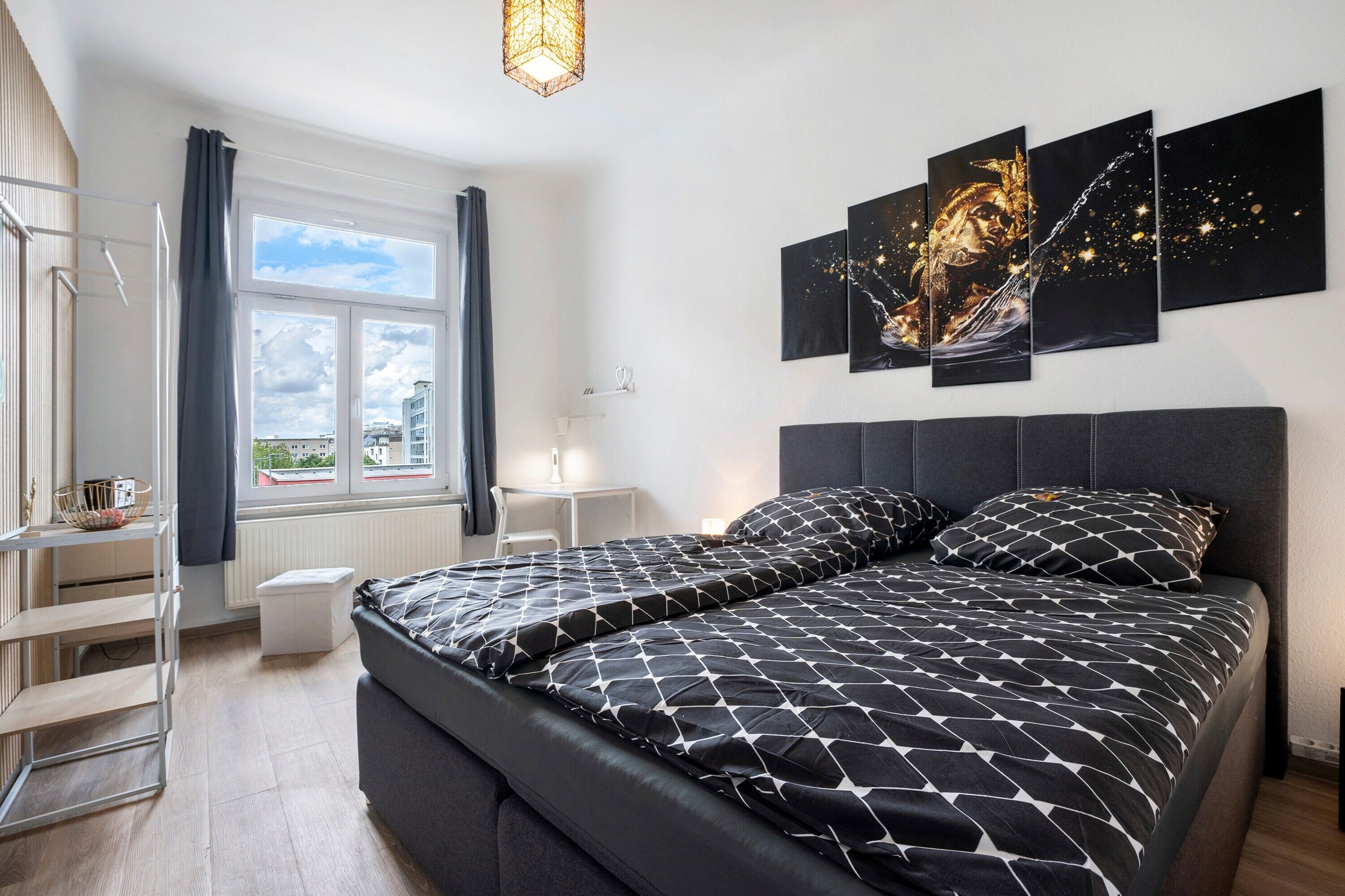 A bedroom with a bed, a window, a bedside table, and a wall with artwork.
