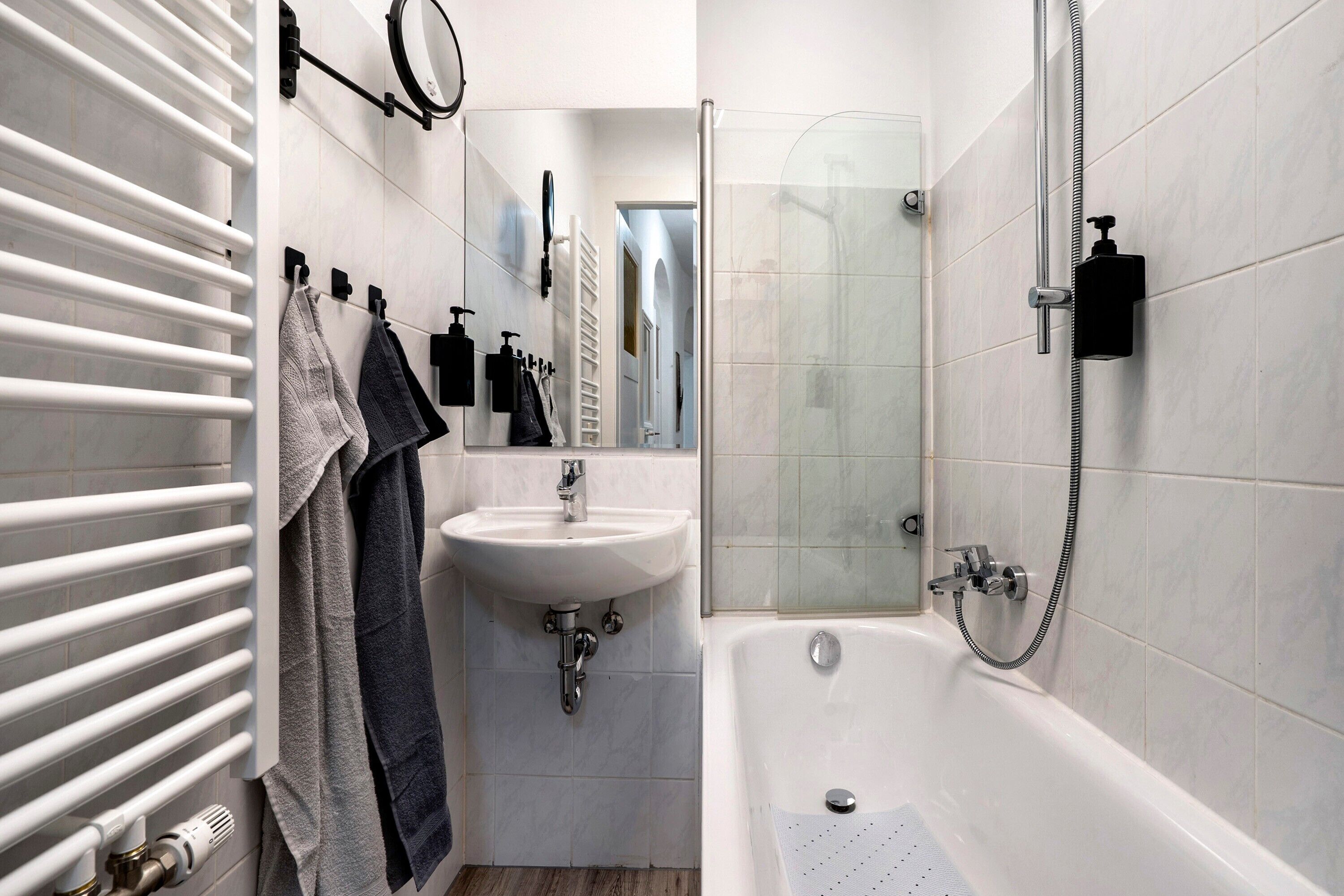 A bathroom with a white bathtub, a sink, a towel rack with towels, and a glass shower enclosure.