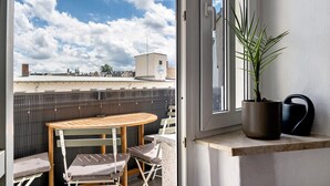 Ein Balkon mit Tisch und Stühlen, einem Blumentopf und einem Fenster mit Blick auf eine Stadtlandschaft.