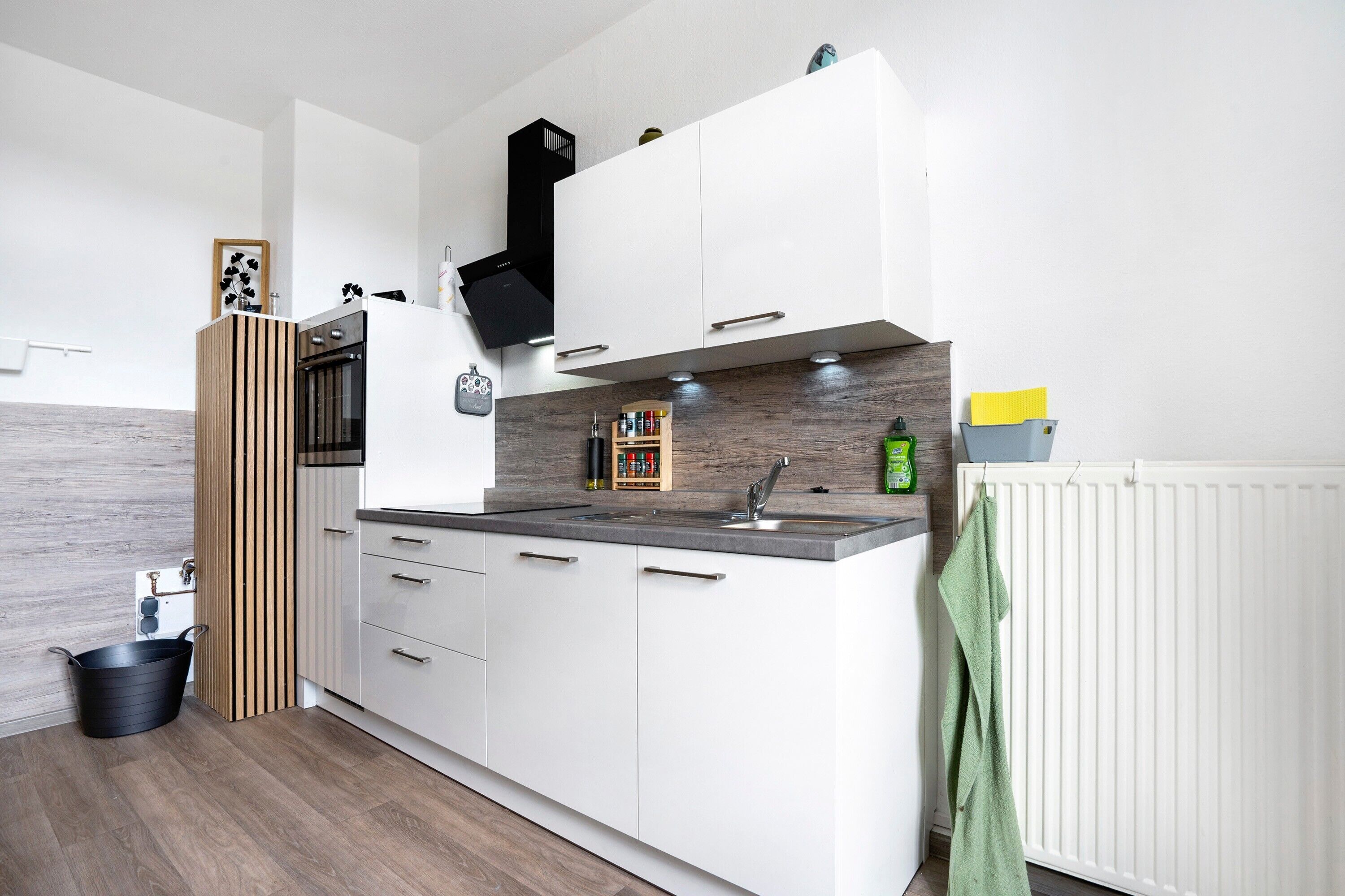 A modern kitchen with white cabinets, a black range hood, a wooden backsplash, and a white radiator.