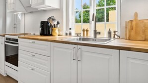 A modern kitchen with white cabinetry, a wooden countertop, a built-in oven, a coffee maker, and a window with a view of greenery. - "Øde" - 100m from the sea by Interhome (Svaneke)
