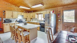 A wooden cabin kitchen with a central island, wooden cabinets, and a refrigerator. - Dubois Riverfront Lodge w/ On-Site Fishing & Views (Dubois)