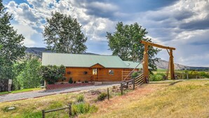 A rustic log cabin with a green metal roof, a wooden porch, and a stone pathway leading to the entrance. - Dubois Riverfront Lodge w/ On-Site Fishing & Views (Dubois)
