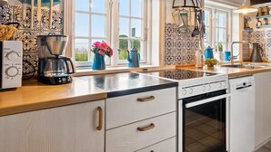 Cocina moderna con una isla grande, encimeras de madera y horno empotrado. Varias ventanas proporcionan luz natural, y los utensilios de cocina están ordenados en estantes.