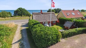 Casa rural con techo de paja, un asta con bandera y vista al mar.