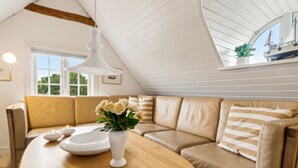 Habitación acogedora y bien iluminada con una mesa de madera, sofá color beige y un amplio ventanal con vista a un barco.